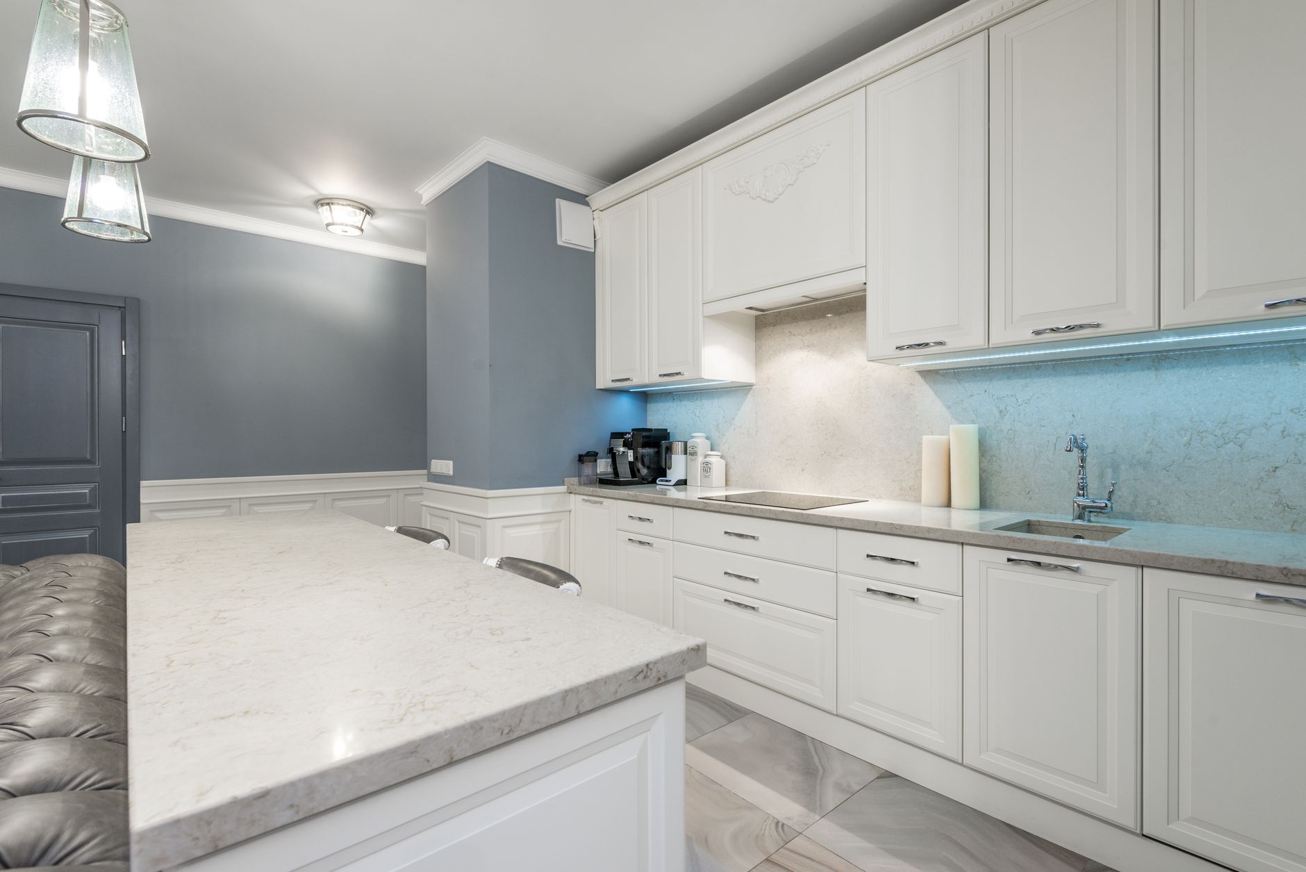 Sleek modern kitchen design featuring white cabinets, marble countertop, and ambient lighting for a in Riverside, CA