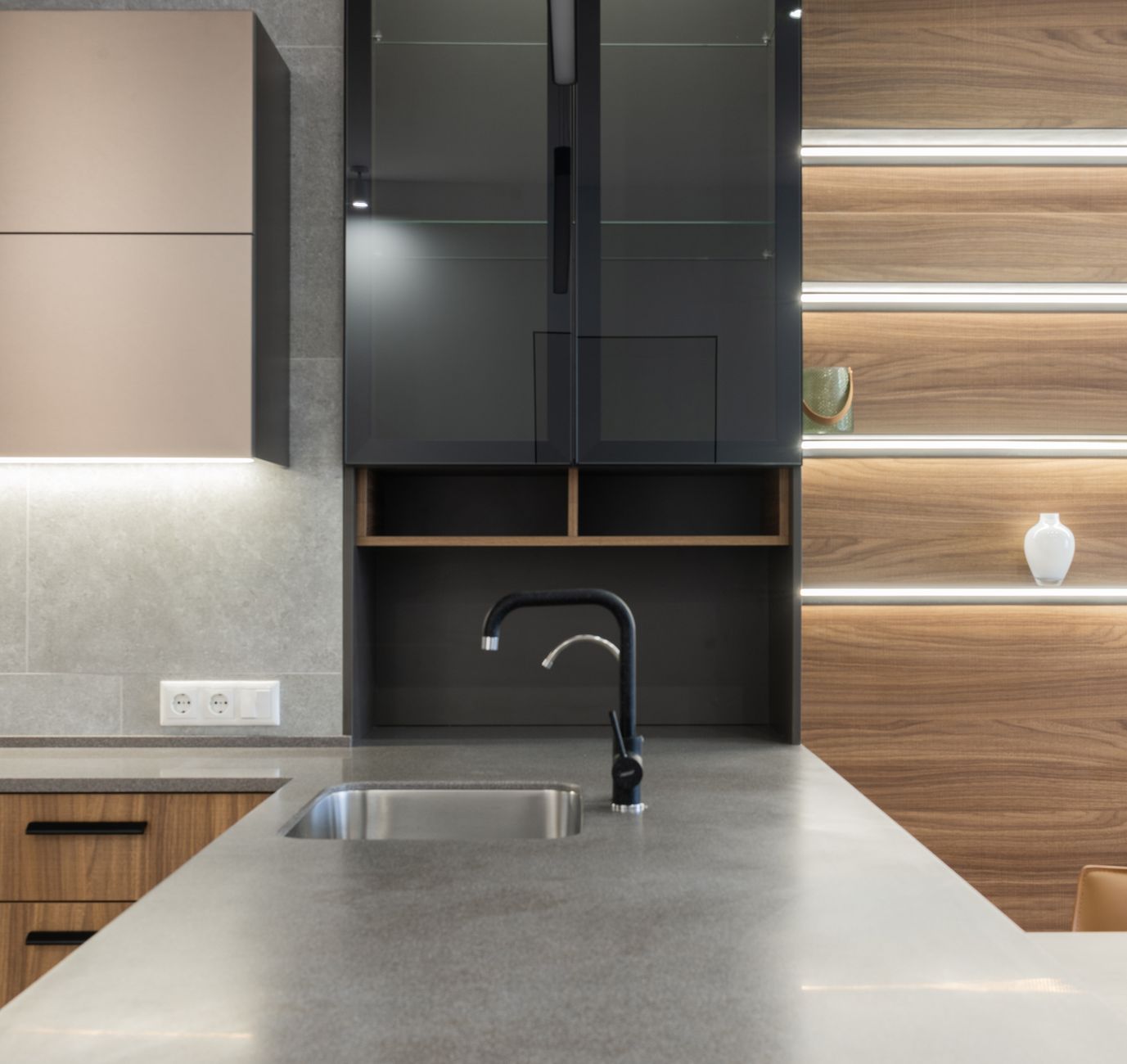 Gray kitchen counter with faucet and sink near cabinets and light decorations on wooden wall in modern in Riverside, CA